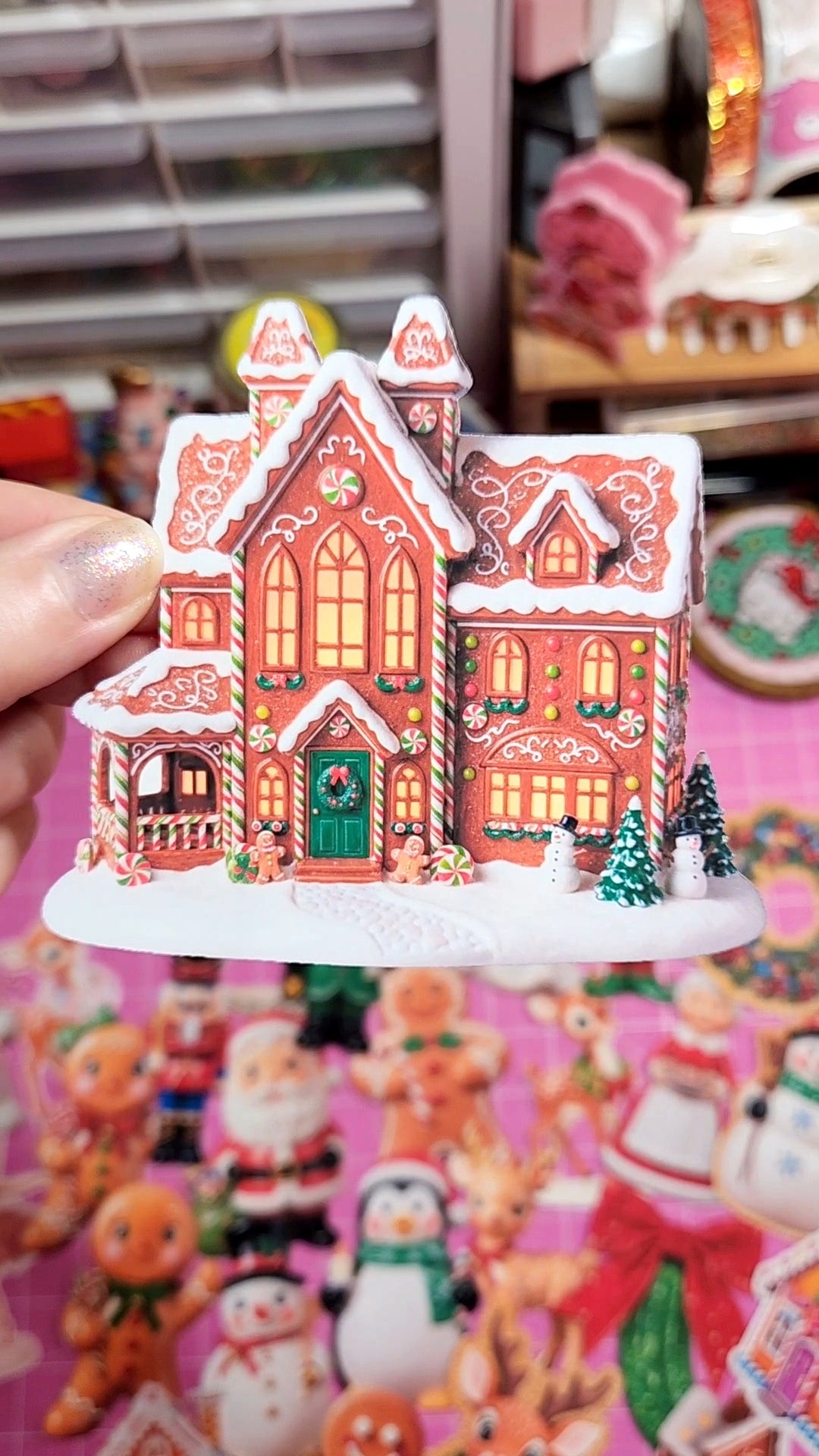 Gingerbread house figurine held in front of a colorful background with Christmas-themed decorations.