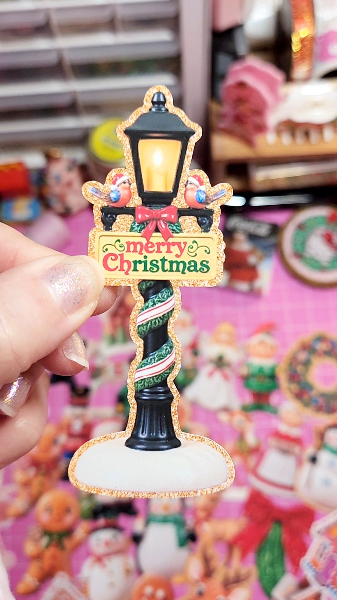 Decorative Christmas street lamp ornament held by a hand with a blurred store background.