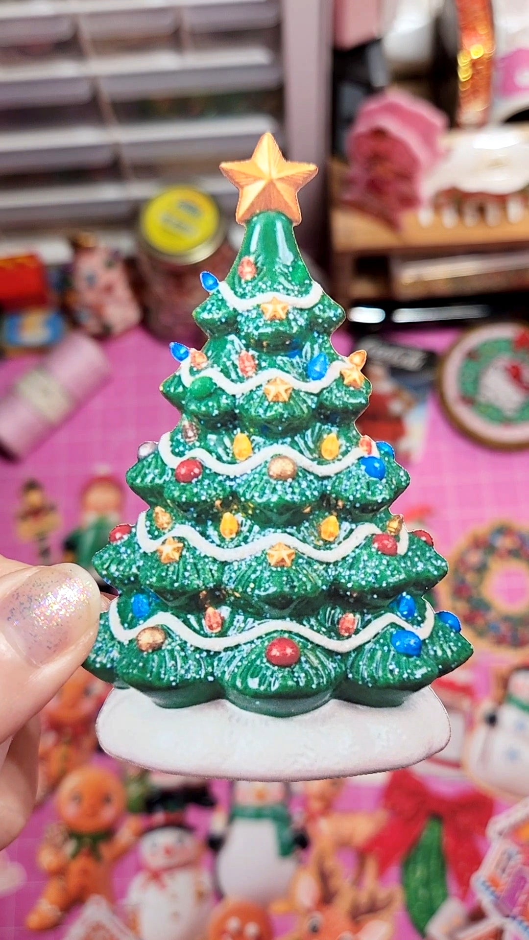 Decorative Christmas tree figurine with colorful lights and a star on top, held in front of a blurred background.