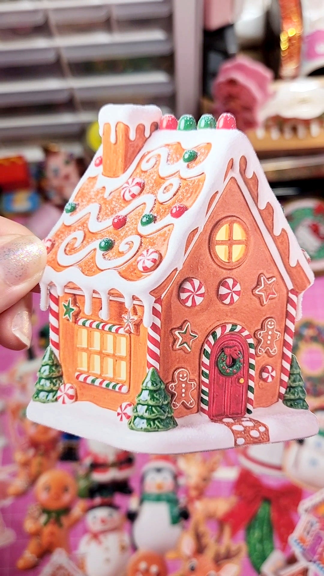 Decorative gingerbread house with colorful roof held by a hand against a blurred background