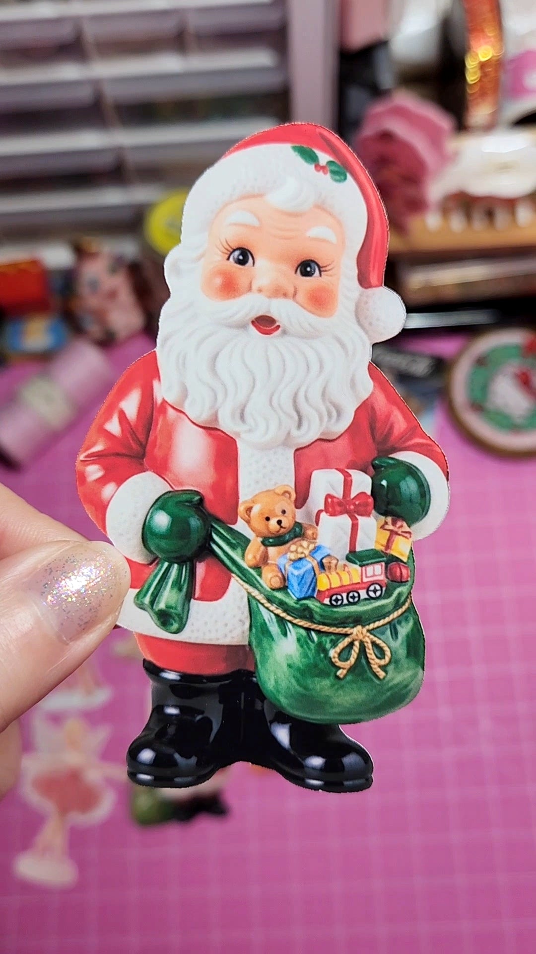 Small figurine of Santa Claus holding a green sack with toys on a pink background