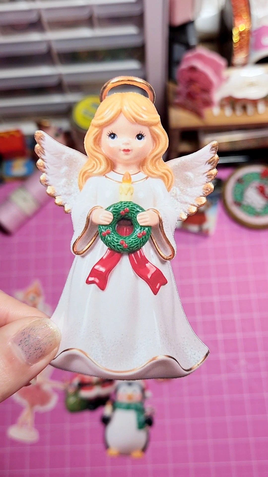 Decorative angel figurine with a wreath held by a hand on a pink background