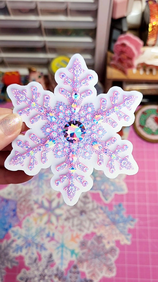 Iridescent snowflake-shaped sticker held by a hand with a blurred background