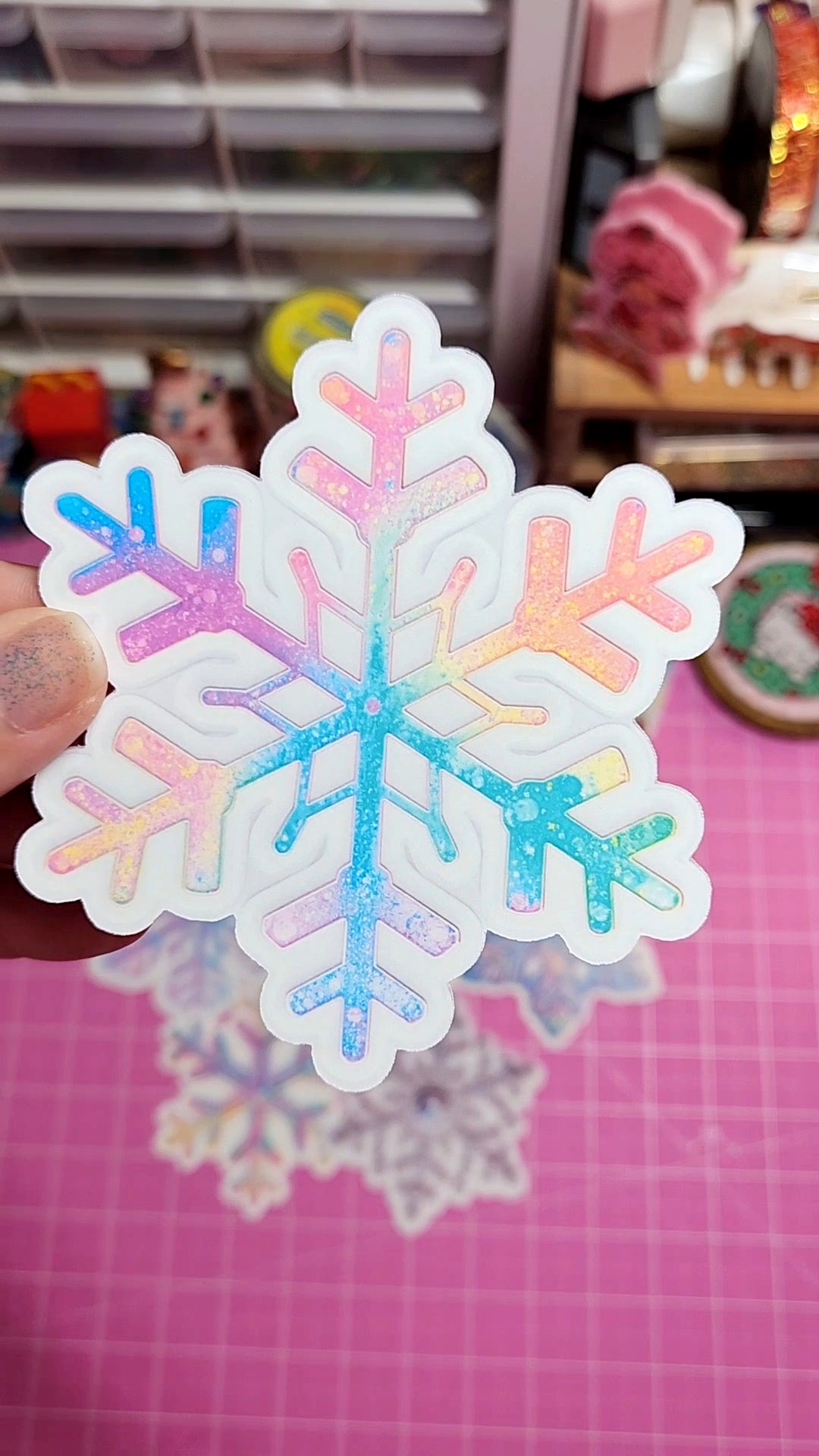 Colorful snowflake sticker held by a hand on a pink surface