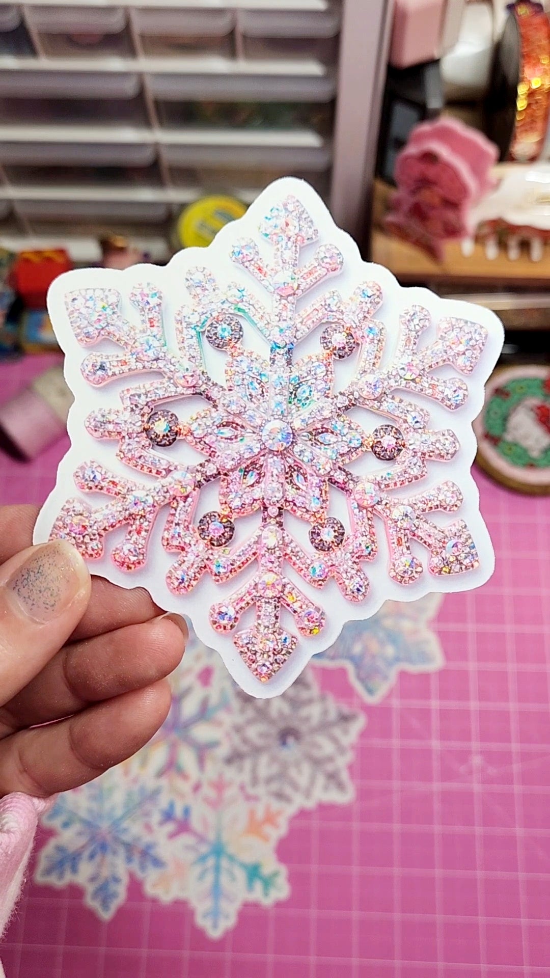 Decorative snowflake sticker with pink and white colors held by a hand on a pink surface.