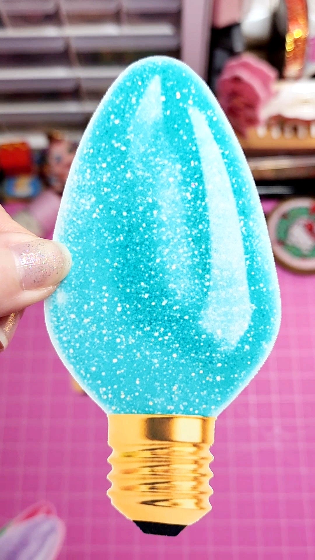 Blue glittery light bulb with gold base held by a hand on a pink background