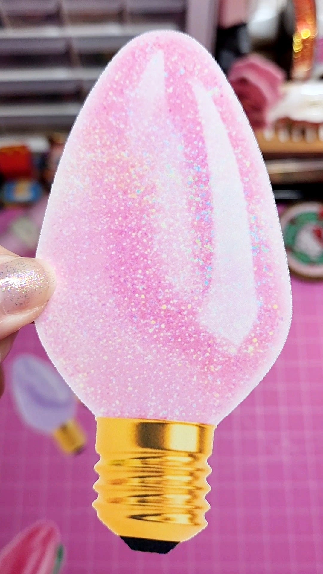 Decorative light bulb with pink and gold design held by a hand against a pink background.