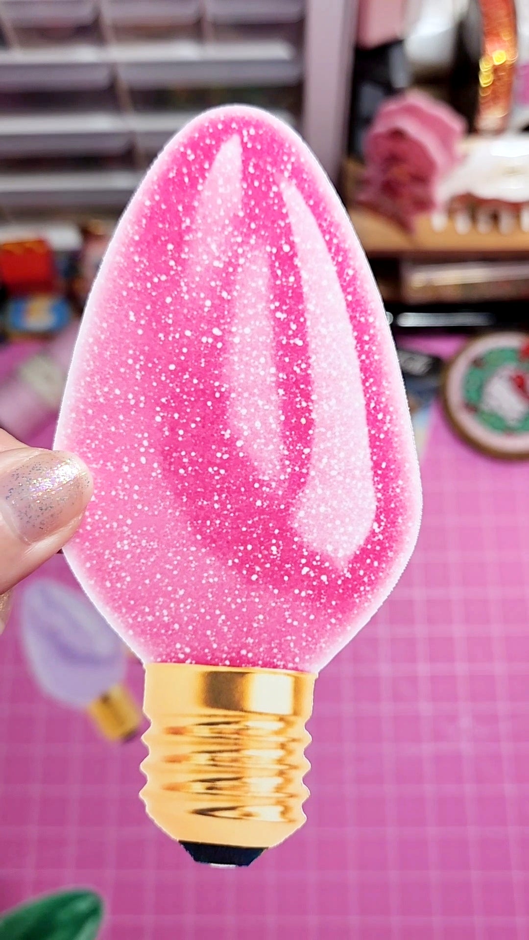 Pink glittery light bulb held by a hand on a pink background