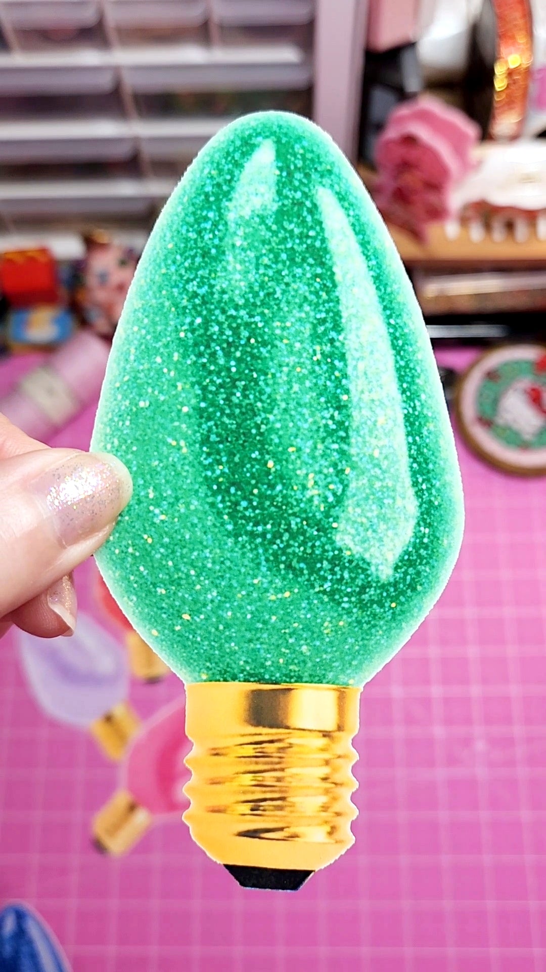 Green glittery light bulb with gold base held by a hand against a colorful background