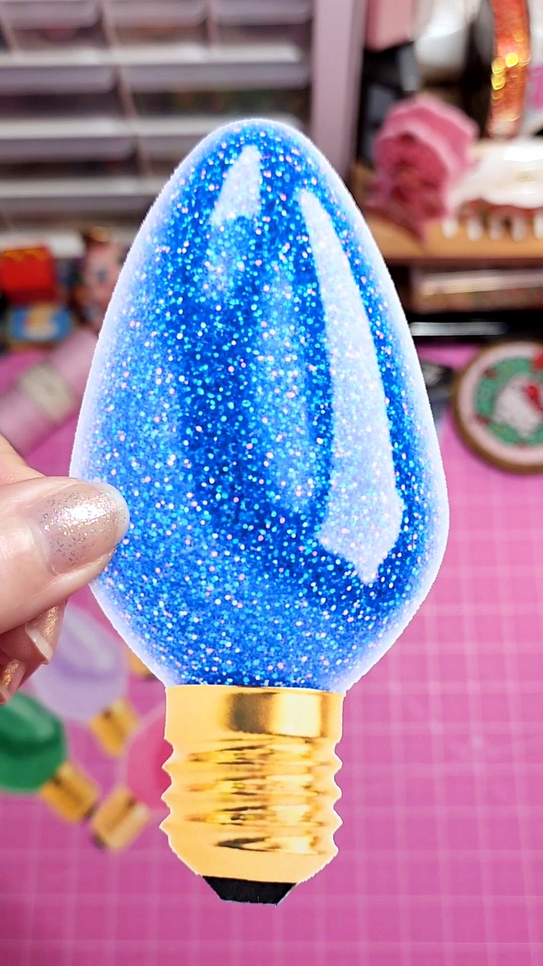 Decorative light bulb with blue glittery design held by a hand against a colorful background.