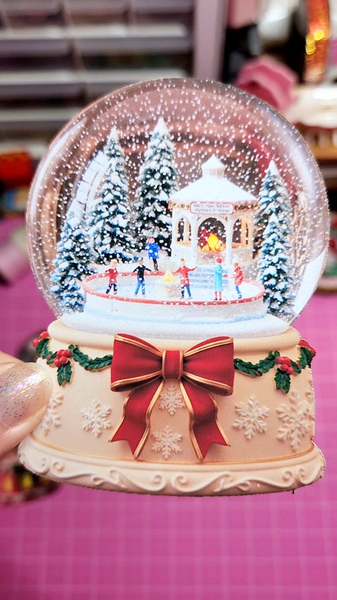 Christmas-themed snow globe with a festive scene inside, featuring a red bow on a pink background.