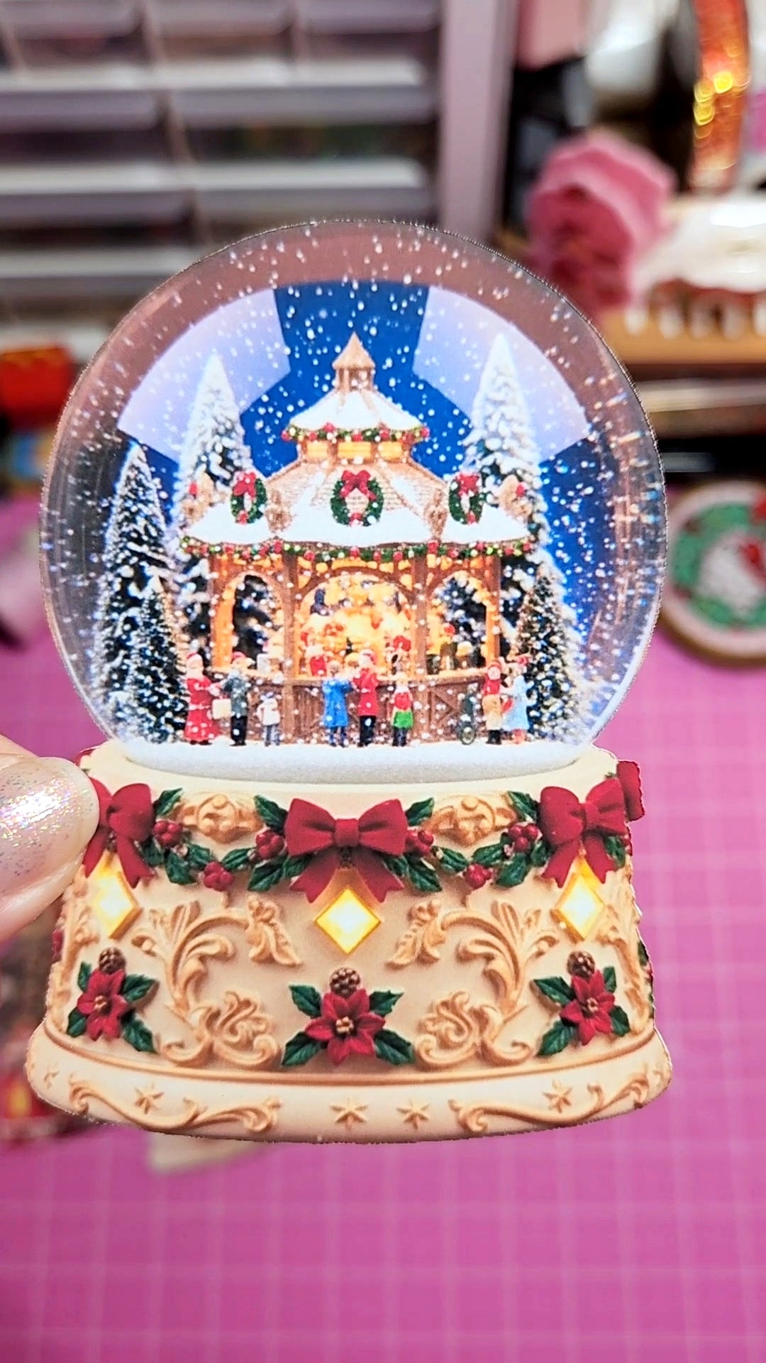 Decorative snow globe with a Christmas scene on a pink surface.