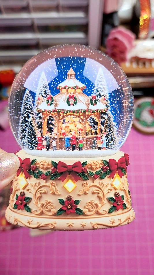 Decorative snow globe with a Christmas scene on a pink surface.