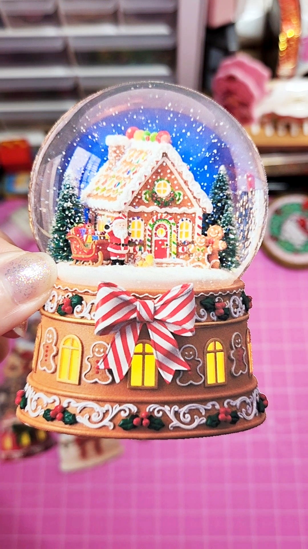 Decorative snow globe with gingerbread house on a pink surface