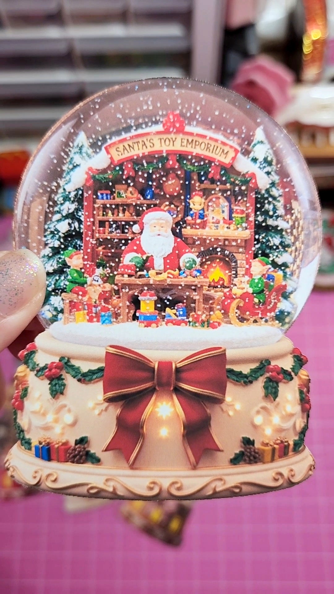 Decorative Christmas snow globe with Santa and toys inside, held by a hand.
