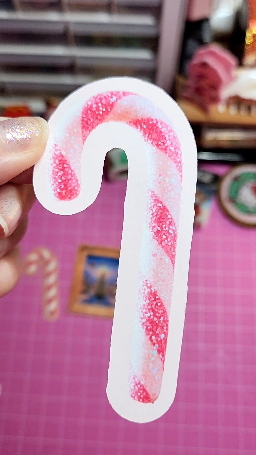 Candy cane-shaped object held by a hand on a pink surface with blurred background