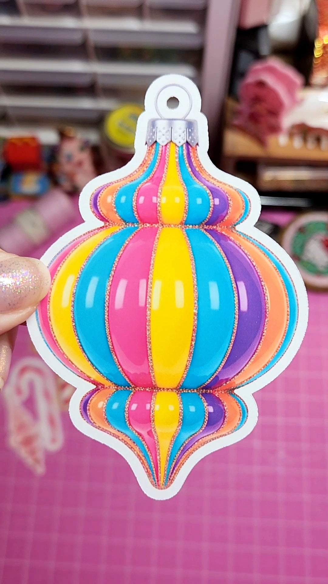 Colorful striped ornament-shaped keychain held by a hand on a pink background