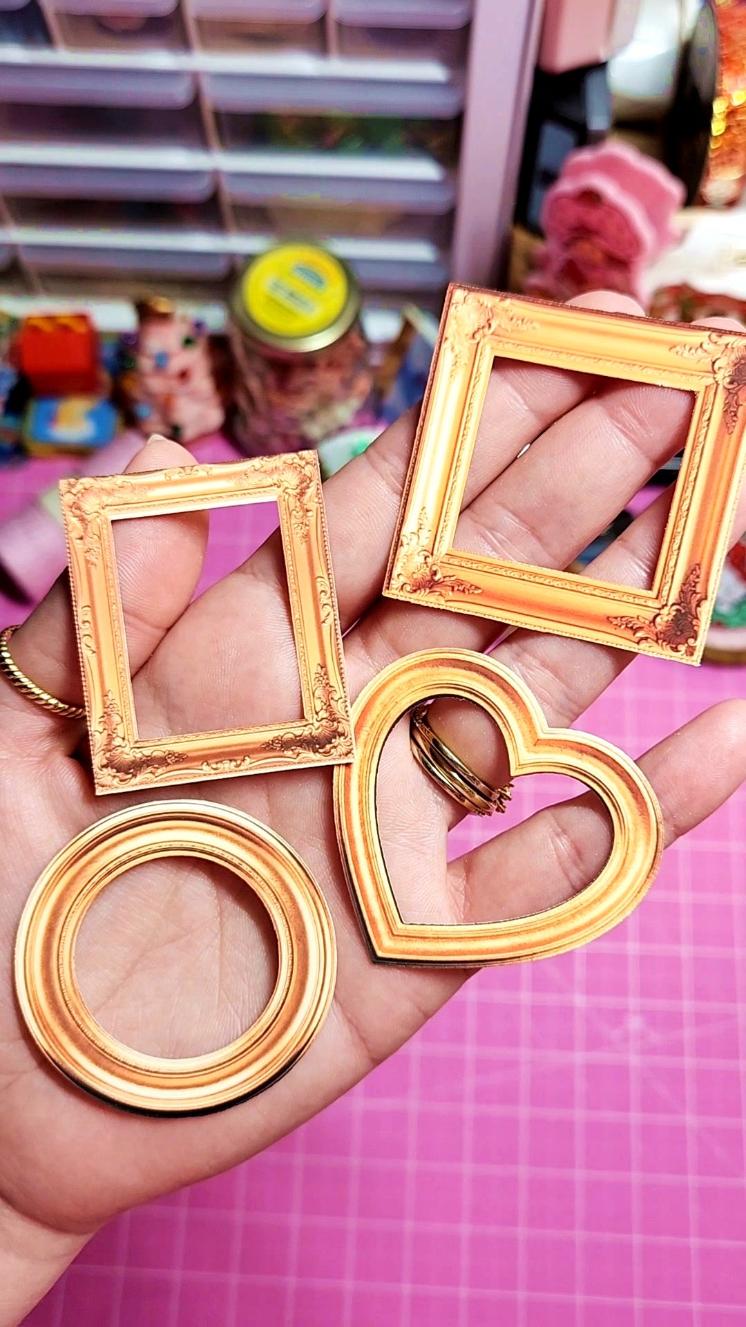 Gold picture frames including square, round, and heart shapes held in a hand with a colorful background.