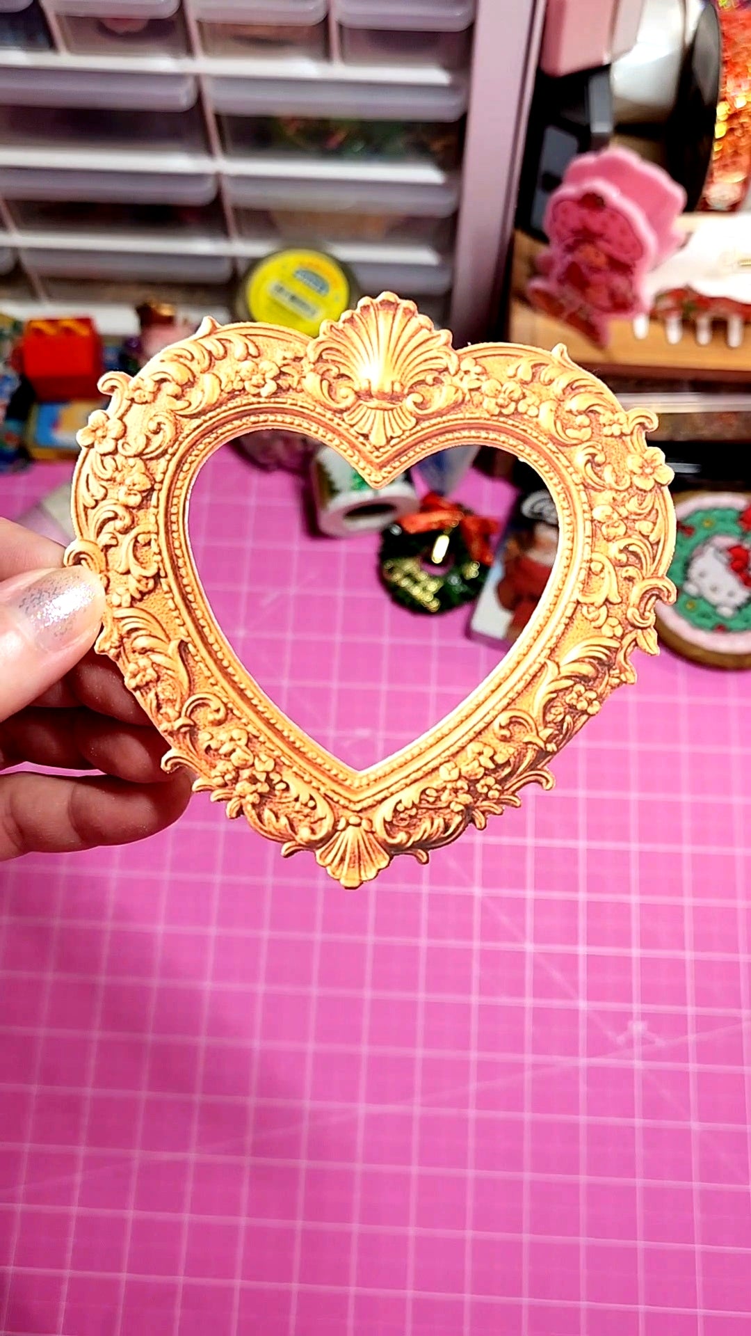 Heart-shaped gold mirror held by a hand on a pink grid background