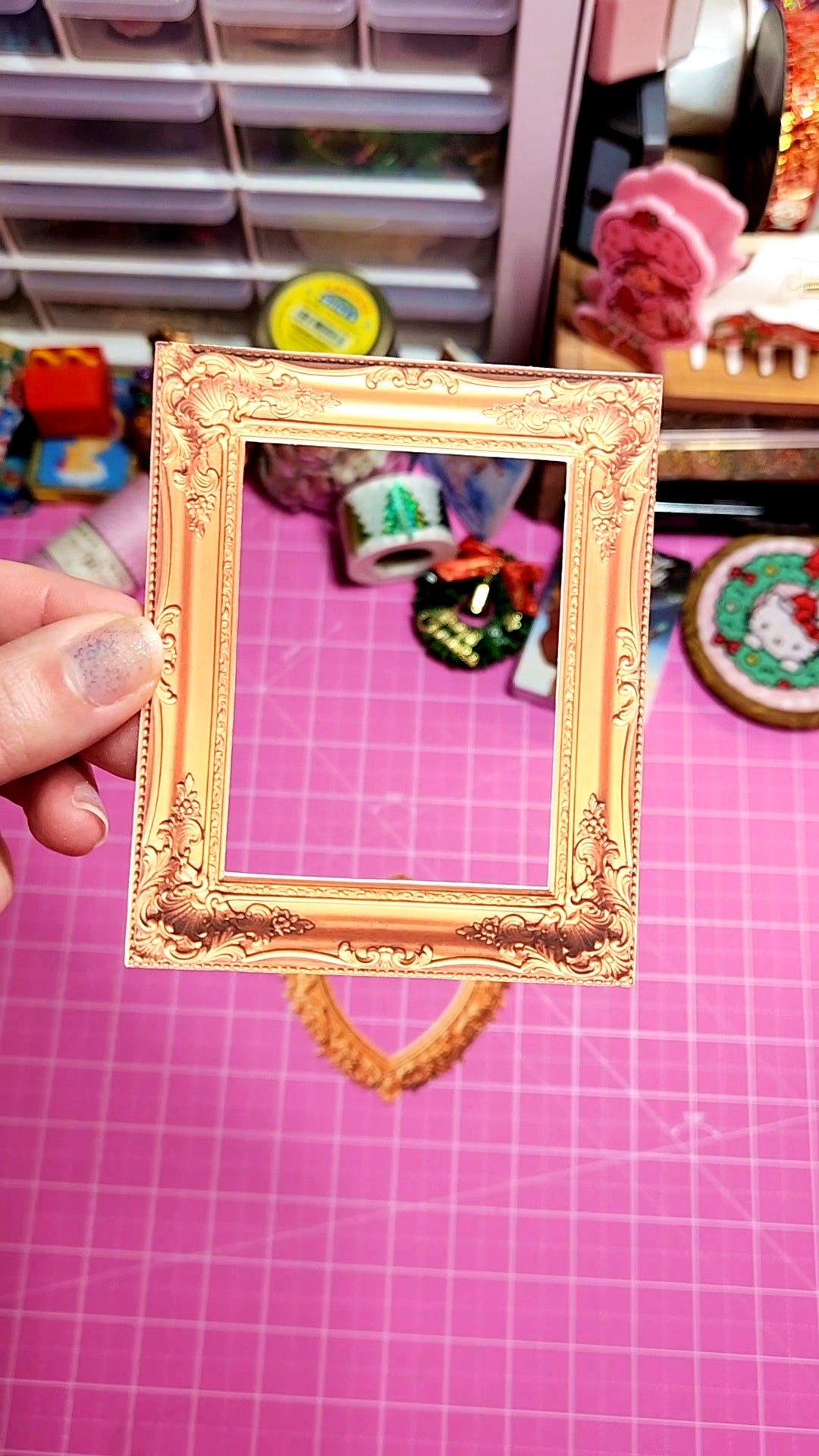 Gold decorative frame held over a pink cutting mat with supplies in the background