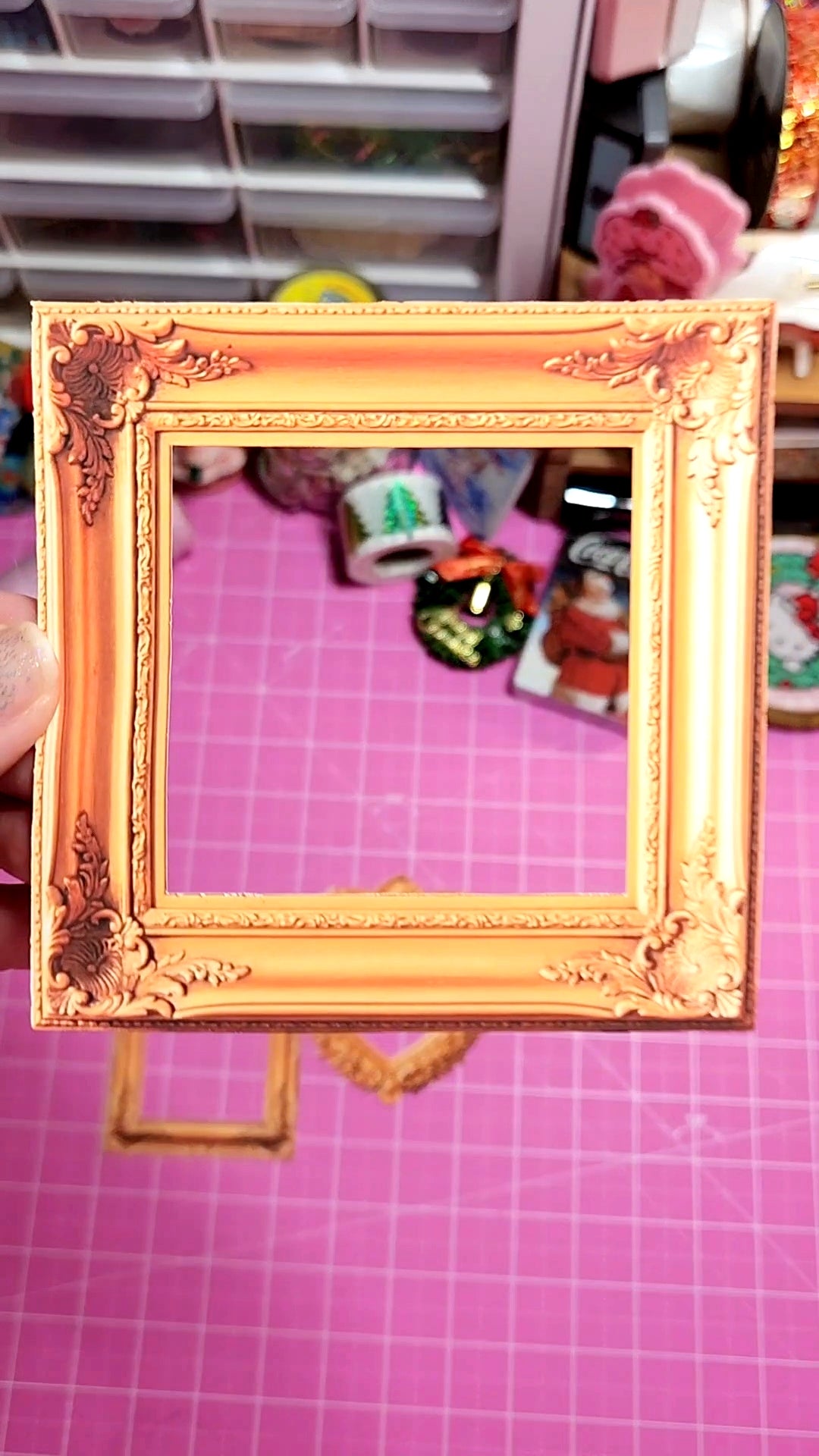 Decorative gold frame held against a pink background with various items.