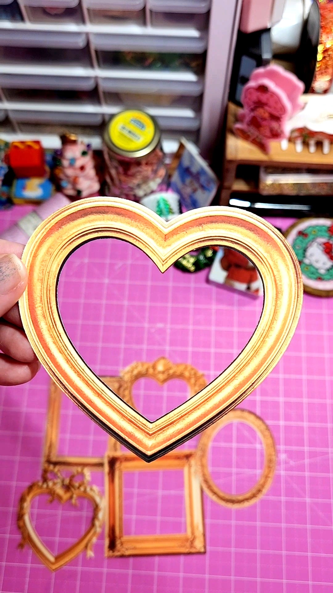 Heart-shaped photo frame held in front of a pink grid background
