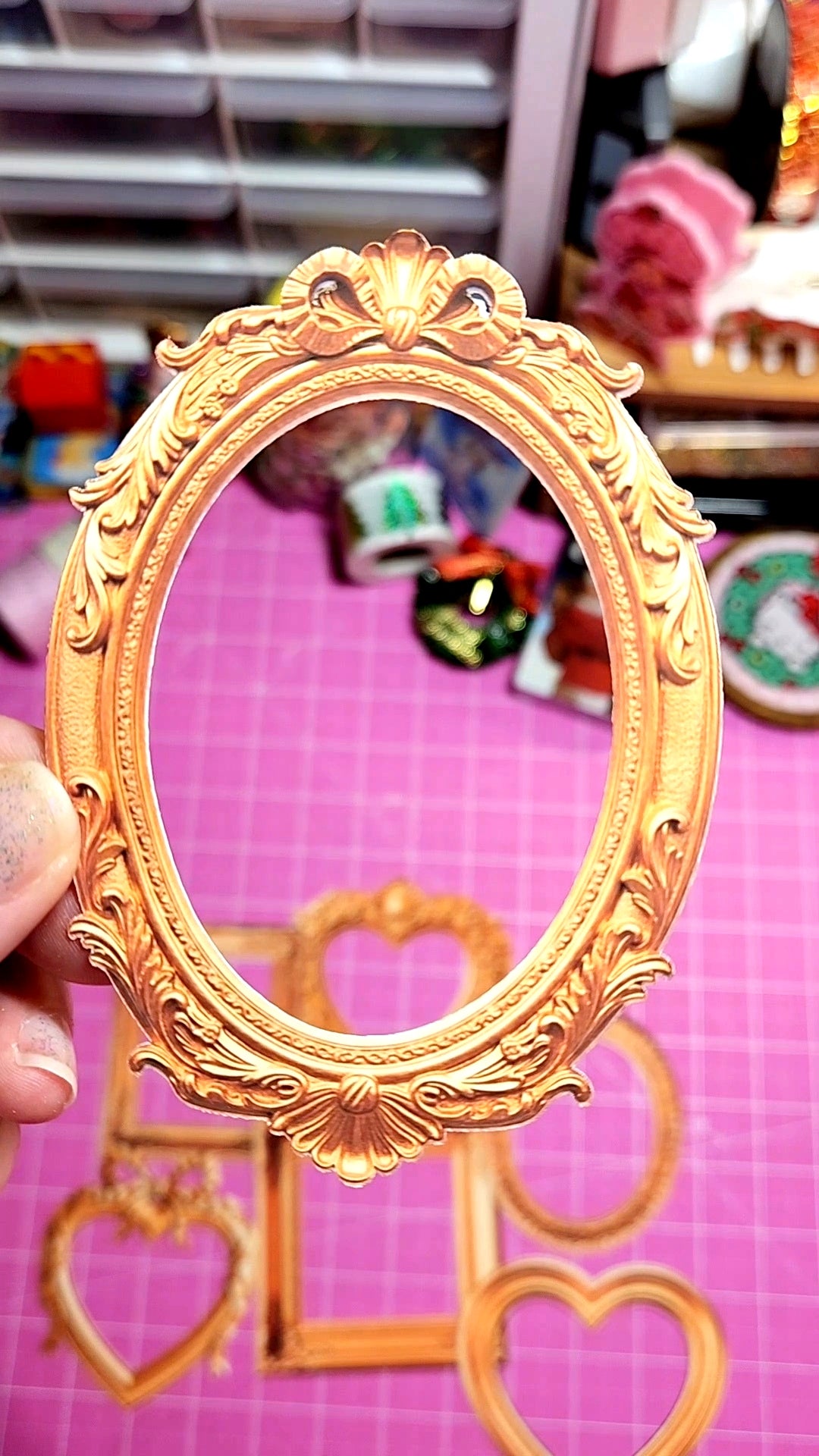 Decorative gold frame held by a hand on a pink background with heart shapes.