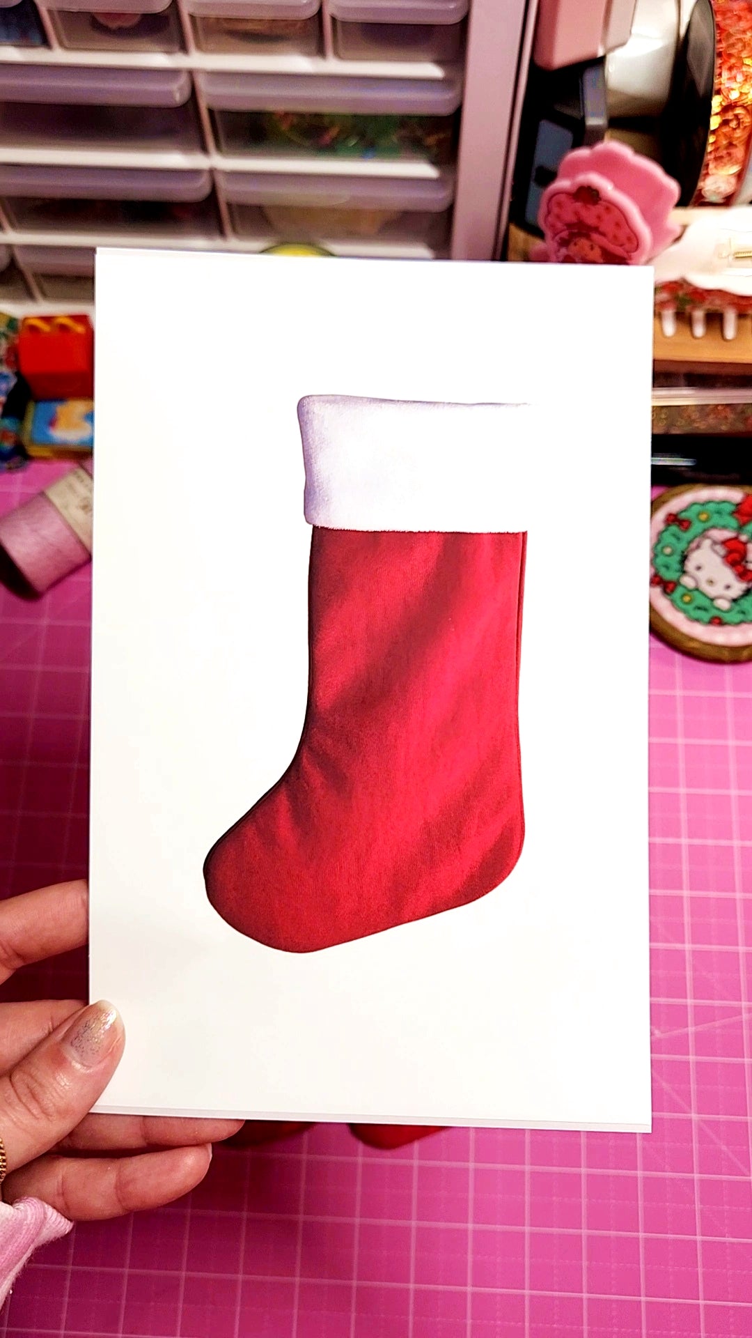 Red Christmas stocking on a white card held by a hand with a pink background
