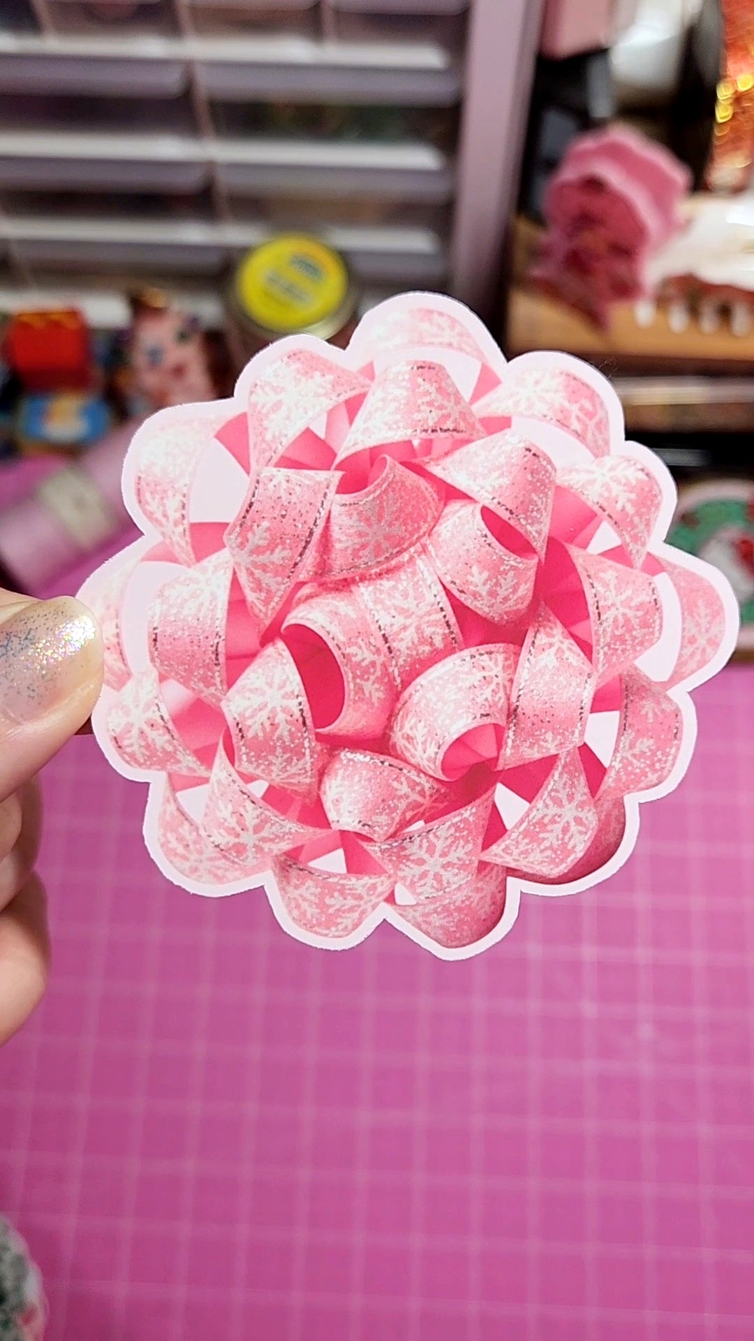 Pink and white decorative item held by a hand on a pink grid background