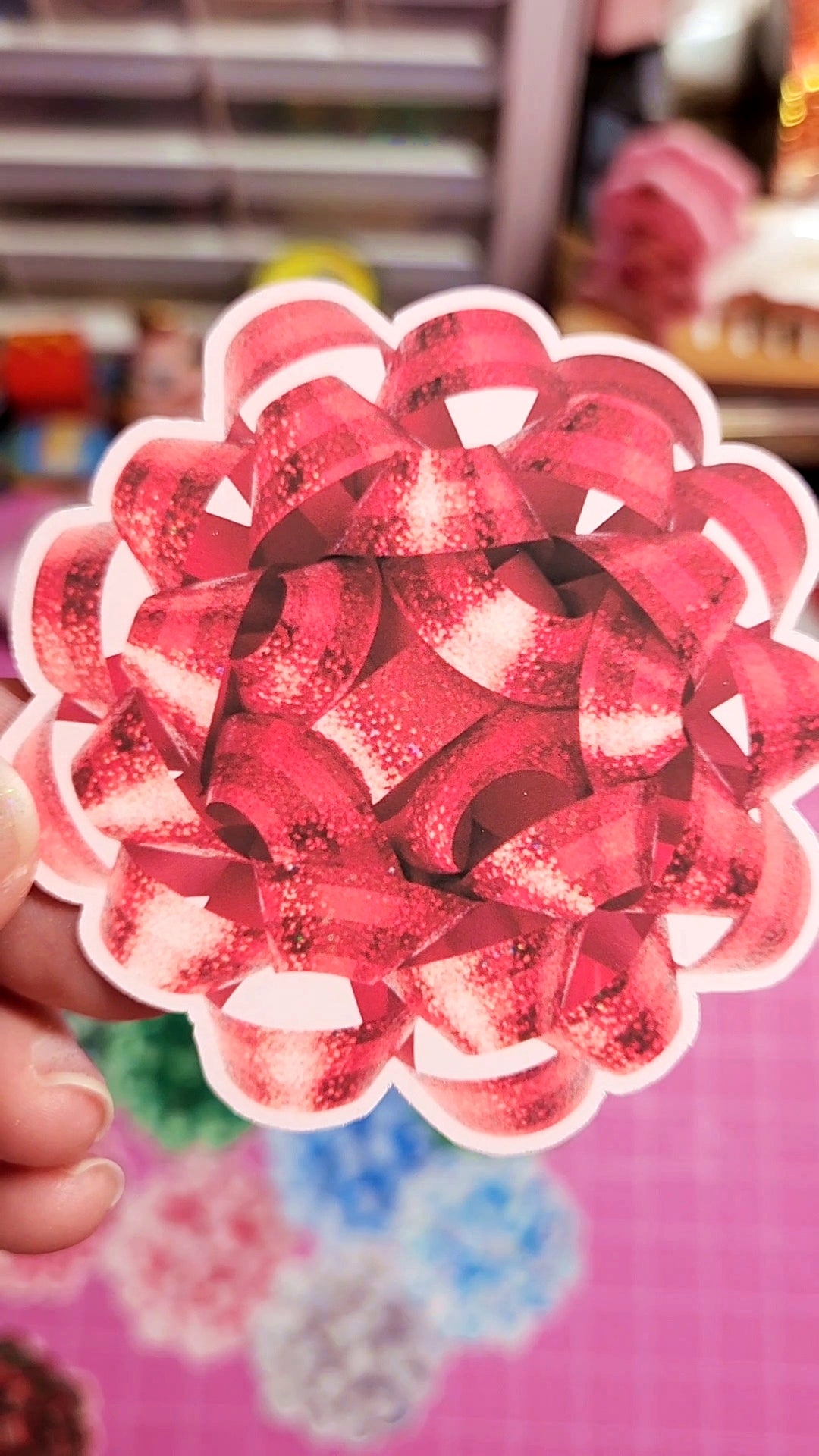 Close-up of a red and white decorative paper flower held by a hand.