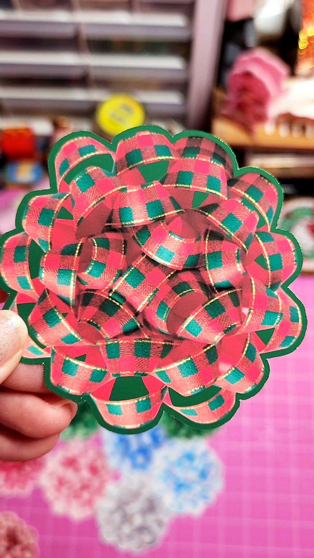 Handmade paper flower with pink and green pattern held by a hand against a blurred background.
