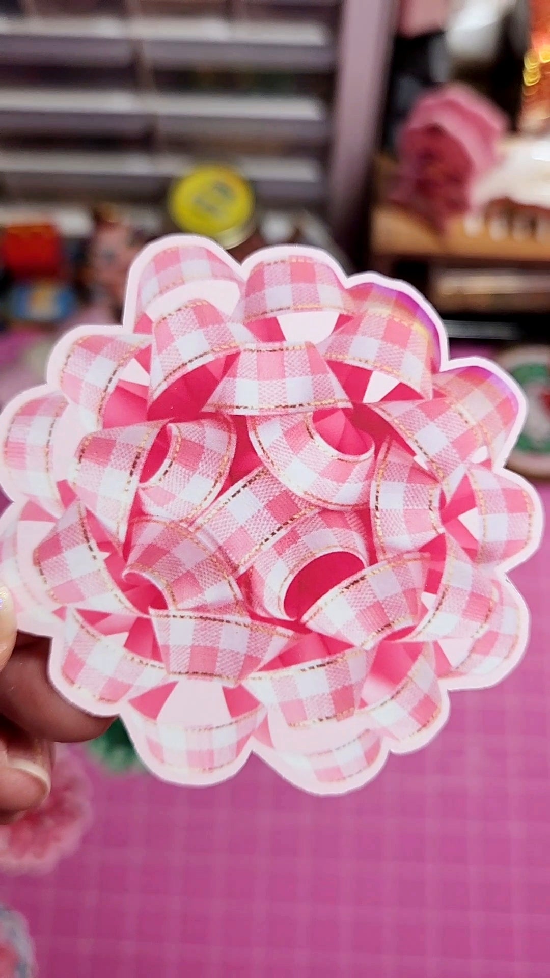 Pink and white checkered flower-shaped object held by a hand on a pink background