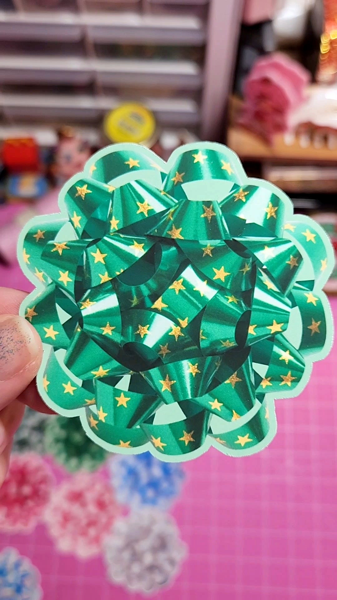 Green and gold decorative paper bow held by a hand with a colorful background