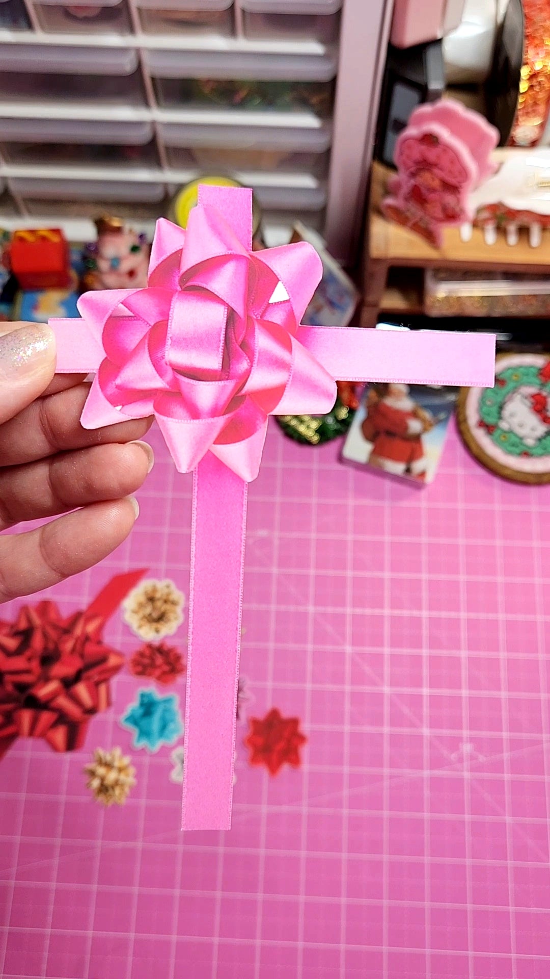 Pink decorative bow held by a hand on a pink grid background