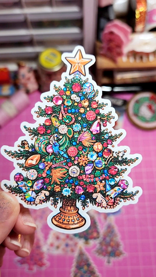 Colorful Christmas tree sticker with decorative elements held by a hand against a blurred indoor background.