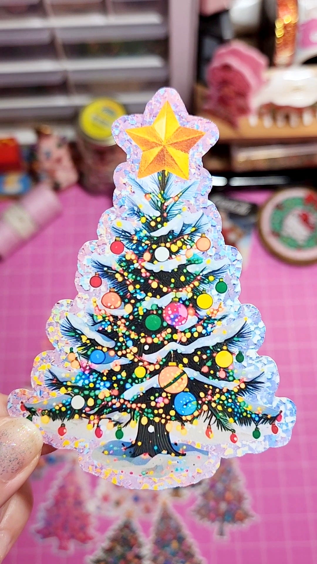 Colorful Christmas tree decoration with a star on top, held against a blurred indoor background.