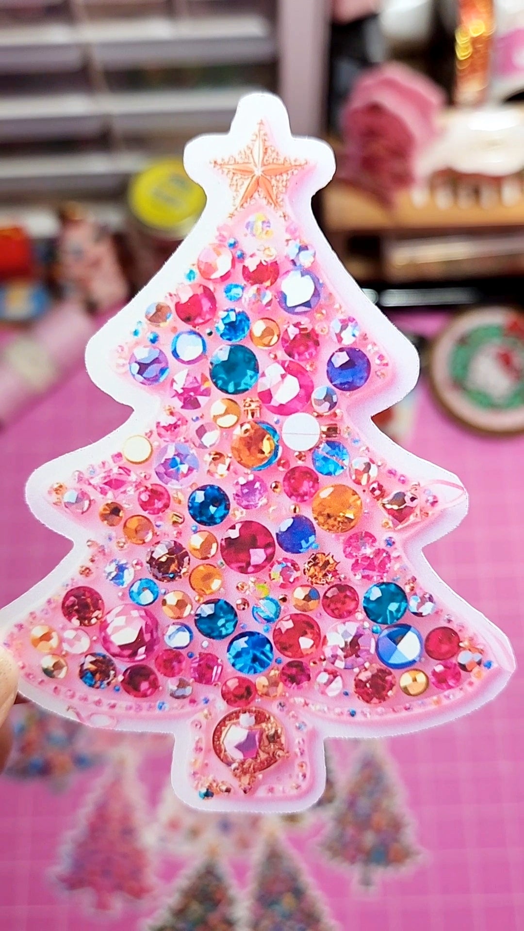 Decorative Christmas tree shaped object with colorful rhinestones on a pink background