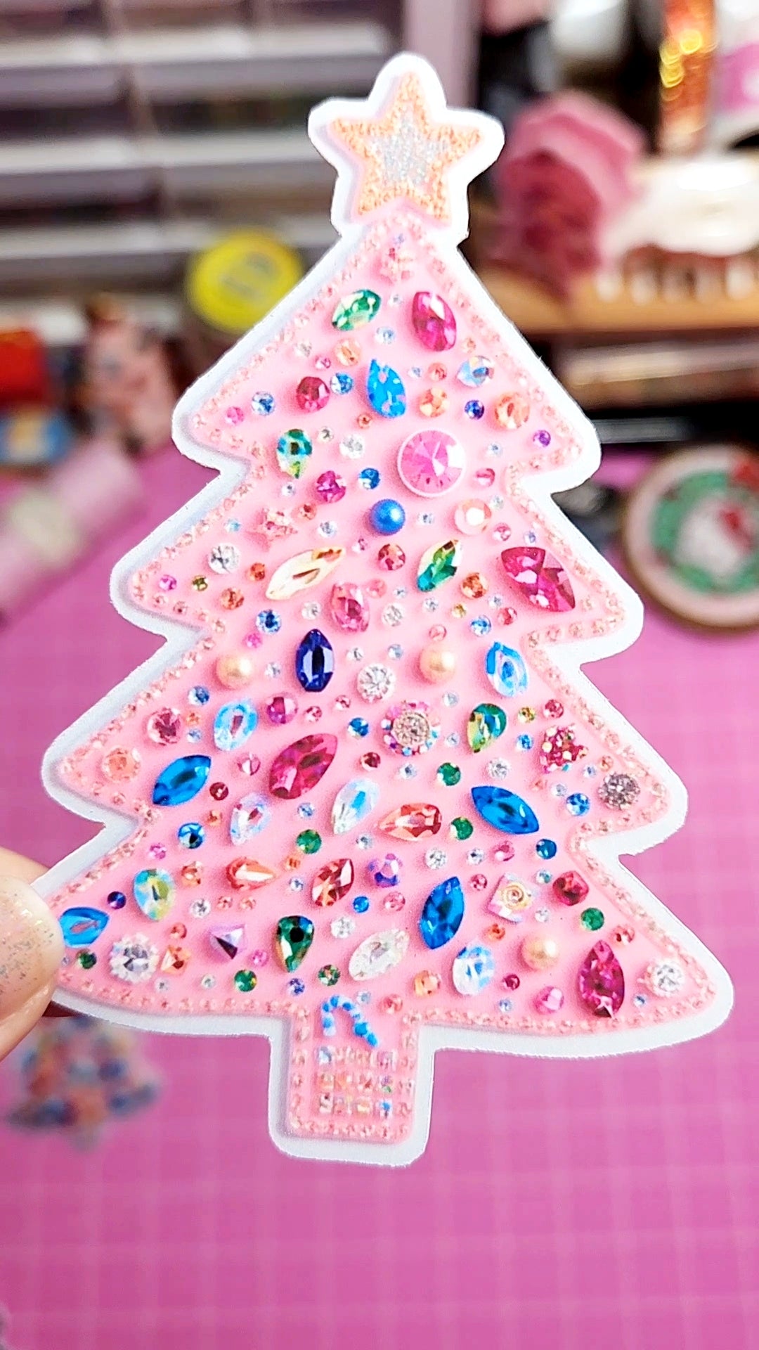 Decorative pink Christmas tree sticker with colorful embellishments on a pink background.