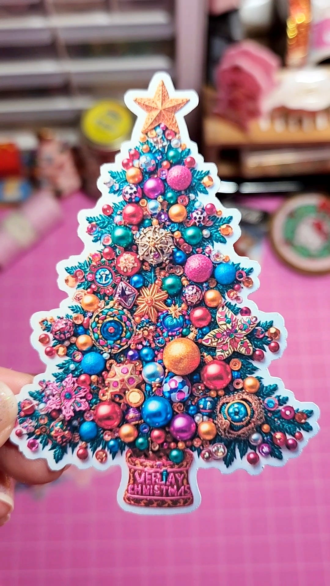 Colorful Christmas tree ornament with decorative beads and a star on a pink background.