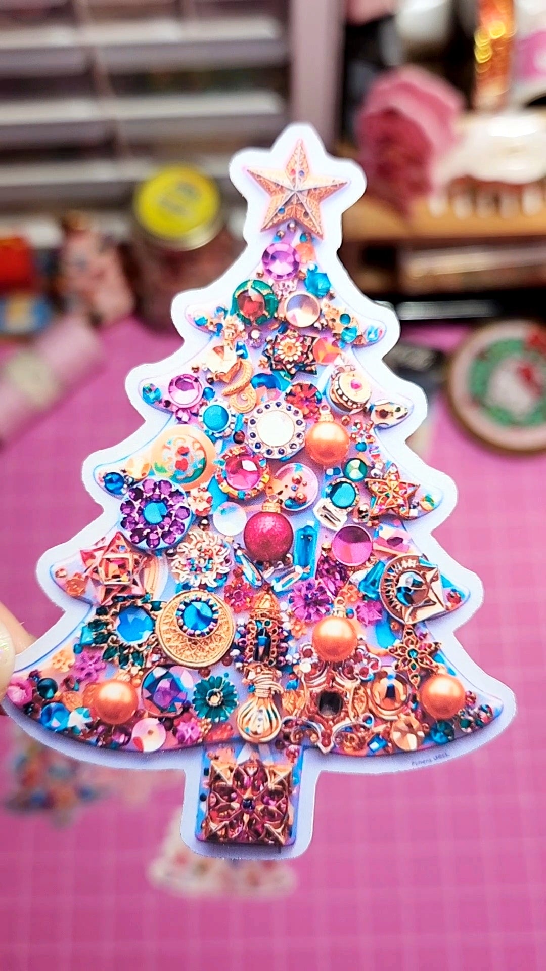 Decorative Christmas tree ornament with colorful rhinestones on a pink surface.