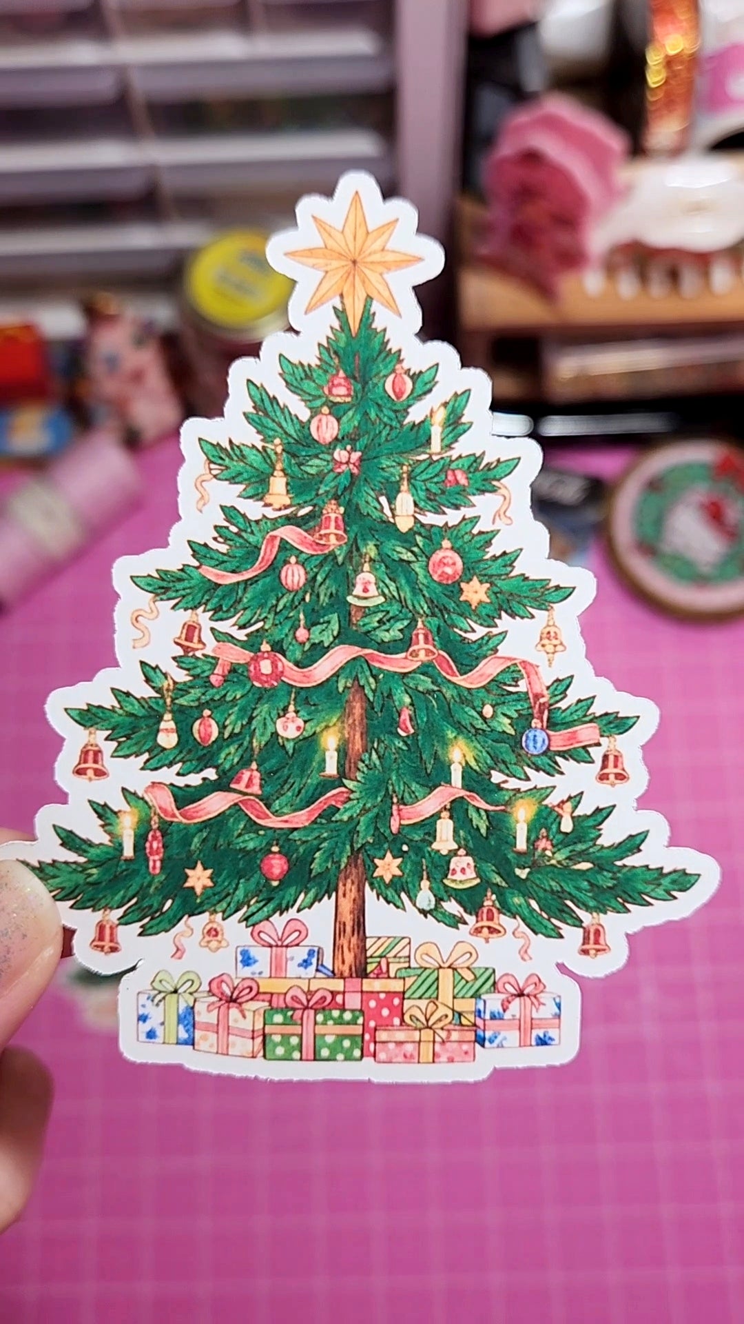 Sticker of a decorated Christmas tree with lights and presents on a pink cutting mat.