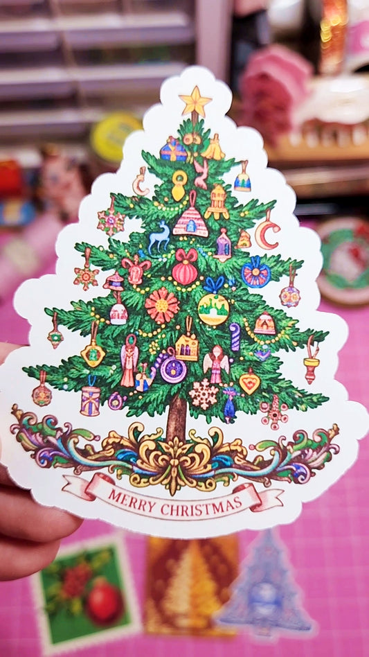 Decorative Christmas tree sticker with colorful ornaments held against a blurred background.