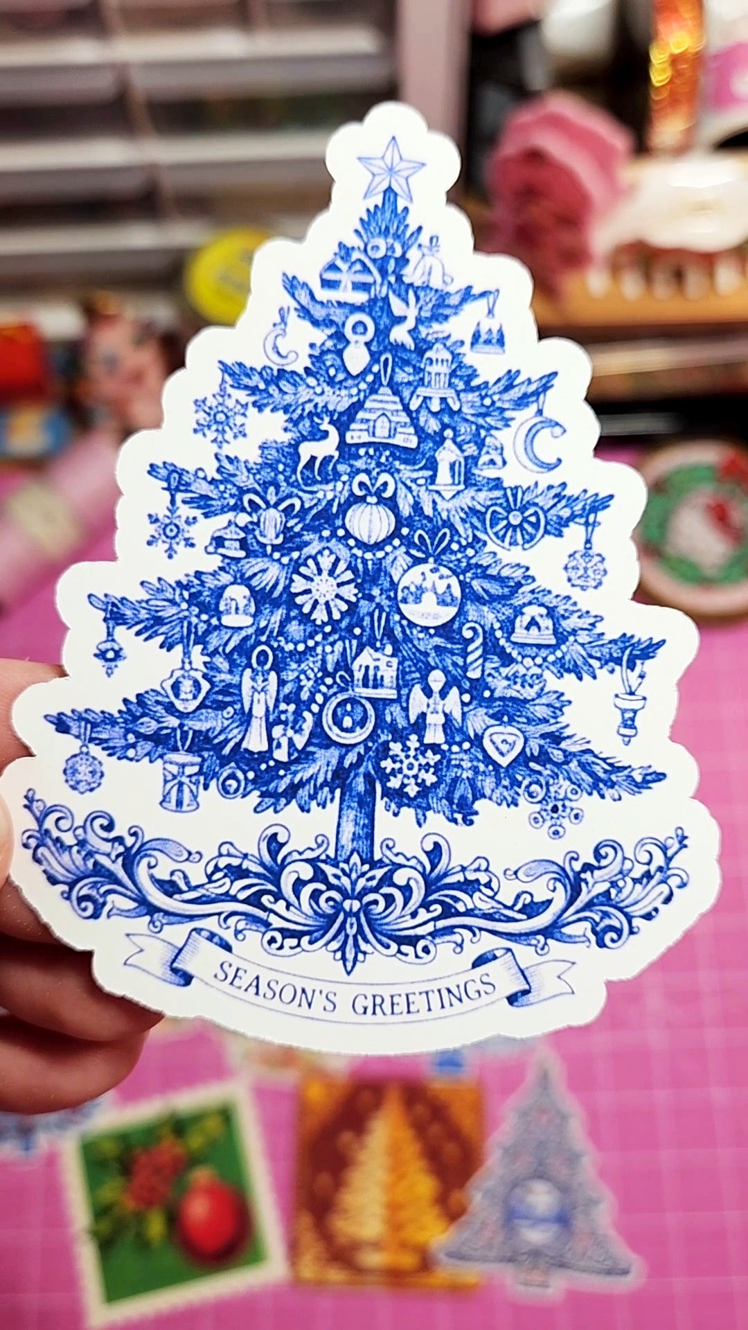 Decorative Christmas tree sticker with blue and white design held against a colorful background.