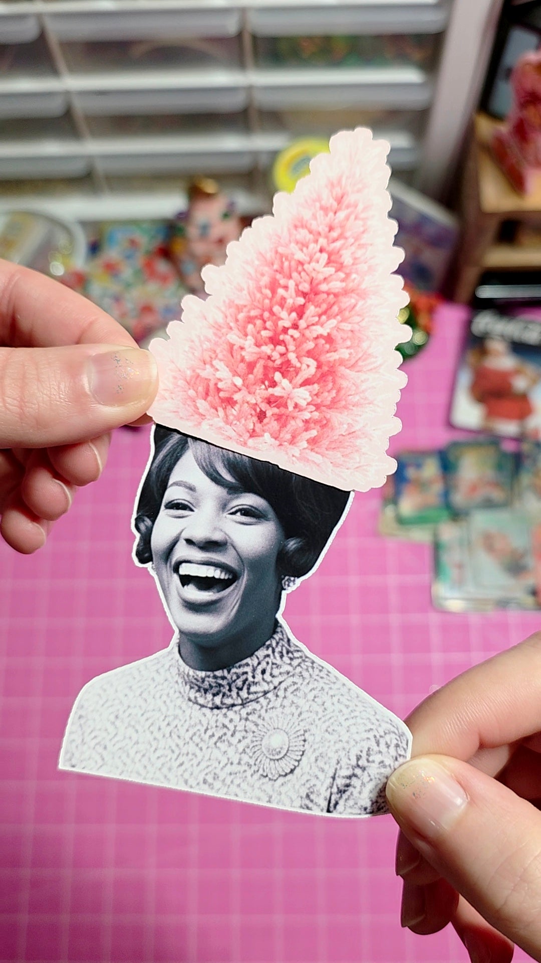 Person holding a cutout of a smiling woman with a pink floral headpiece against a colorful background.