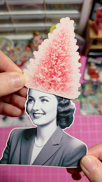 Person holding a cutout of a woman with a pink tree-shaped hat against a pink background