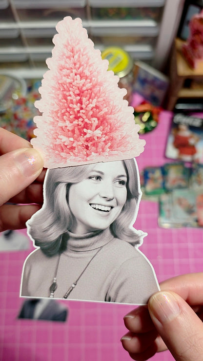Cardboard cutout of a smiling woman with a pink tree-shaped object on her head, held against a colorful background.