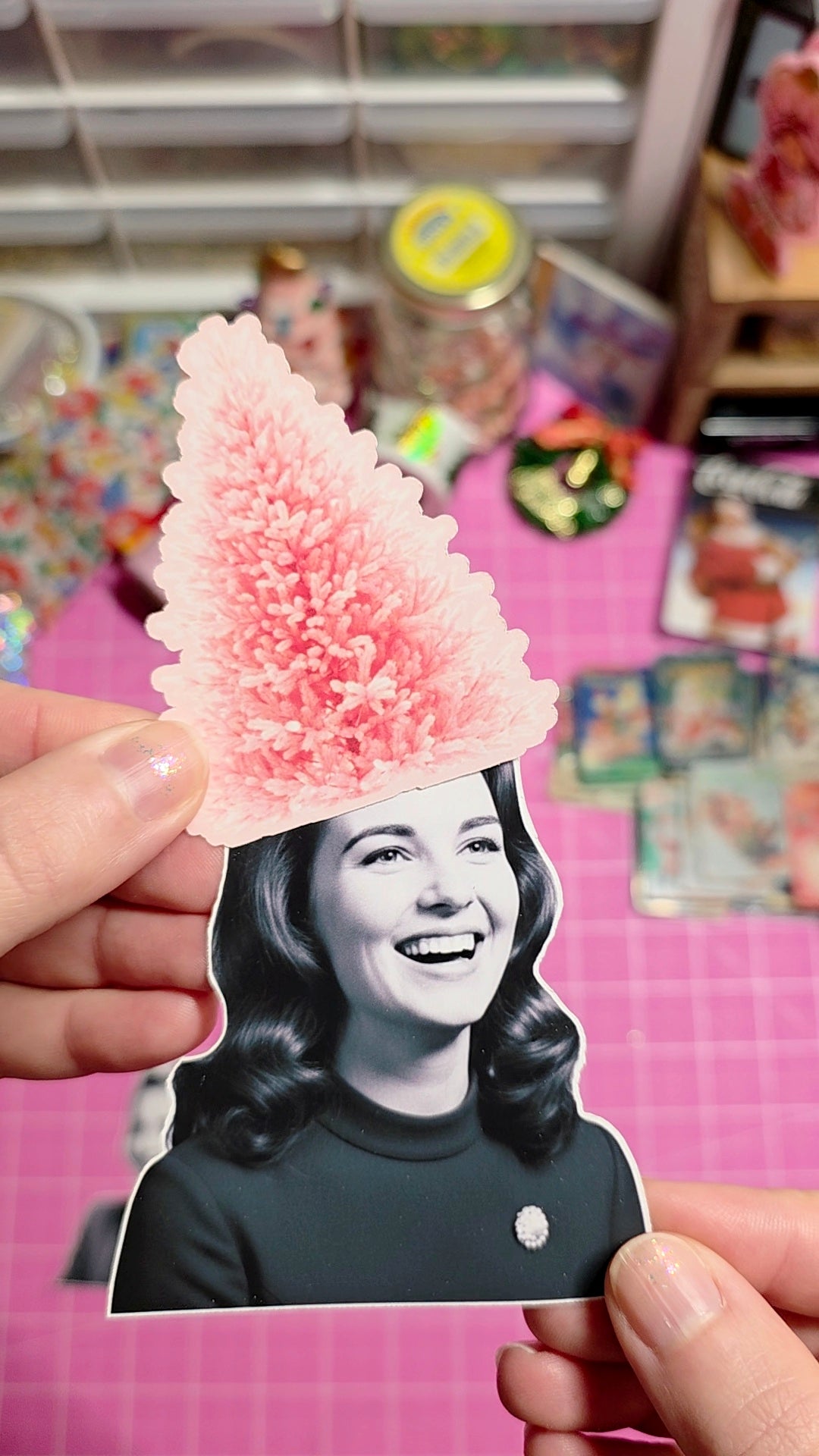 Person holding a cutout of a woman with a pink pom-pom hat against a colorful background.