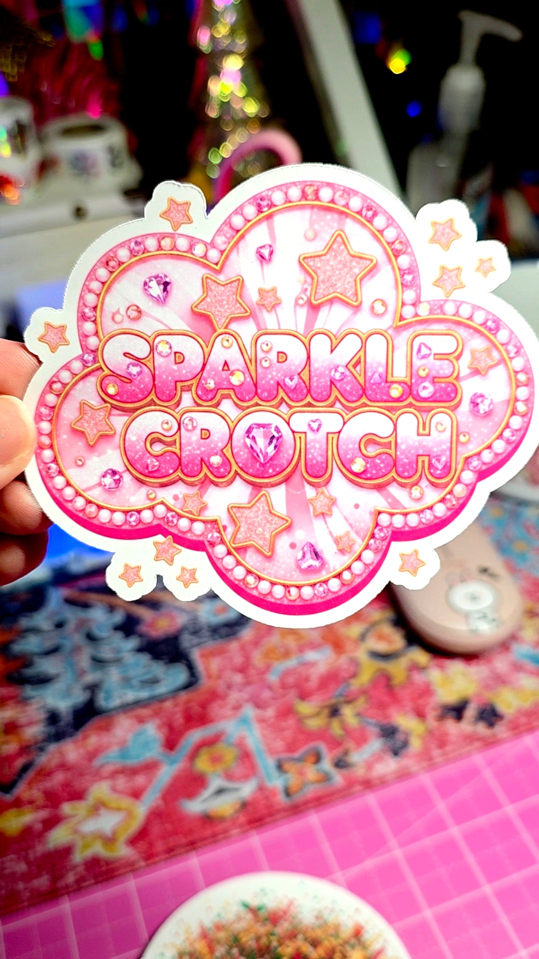 Sticker with 'Sparkle Grotch' text held by a hand against a colorful background