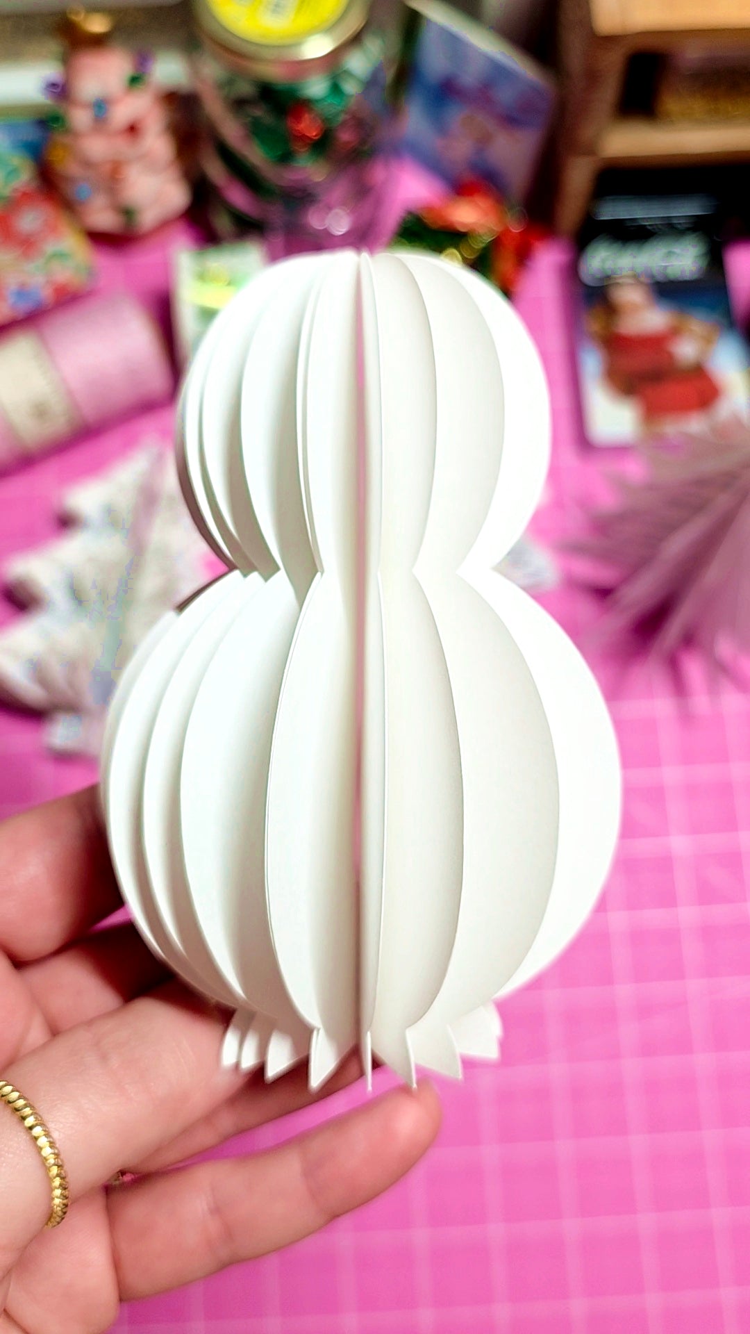 White 3D geometric object held by a hand on a pink surface with colorful background