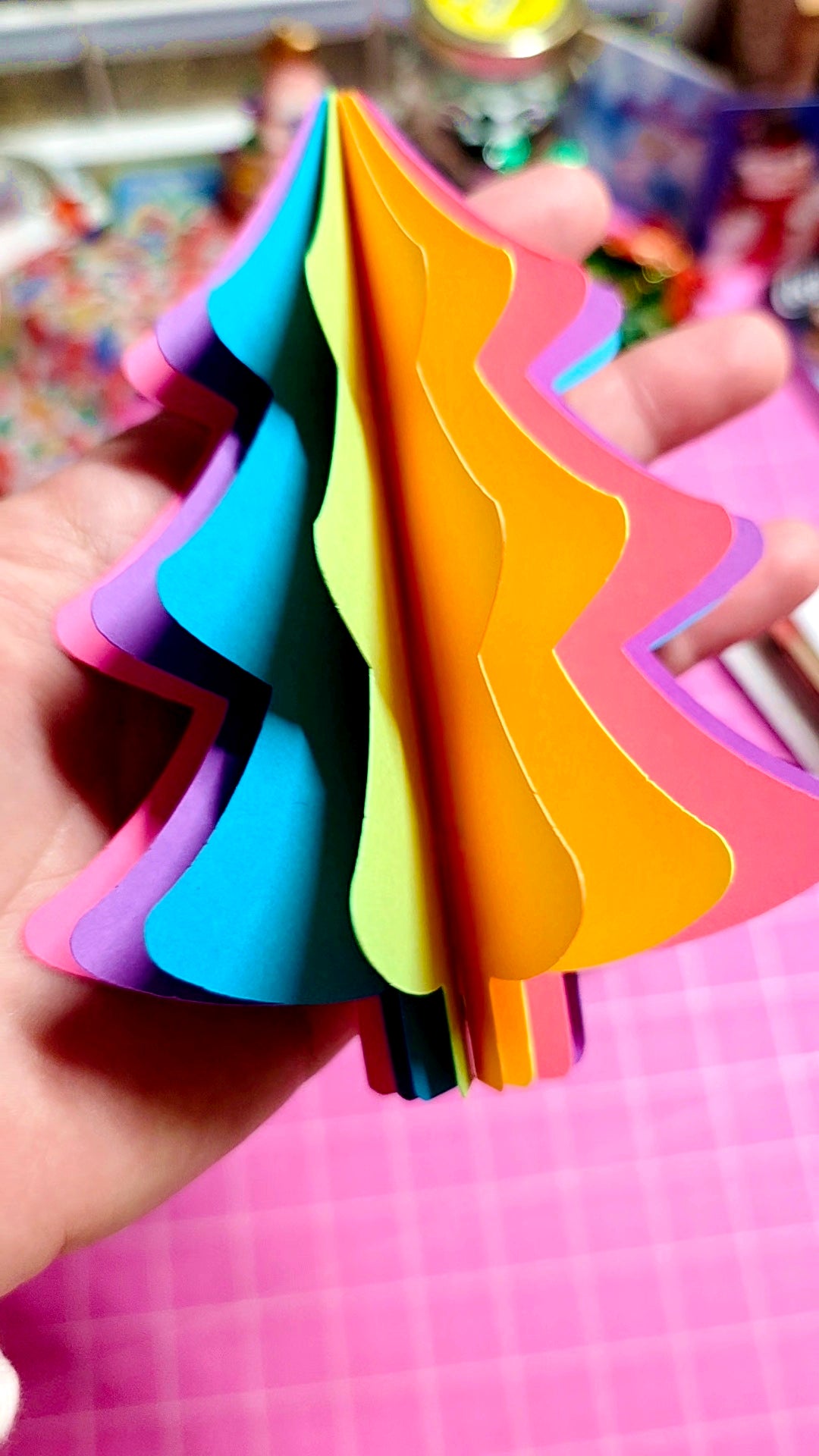 Colorful paper cutouts shaped like triangles held by a hand on a pink surface.